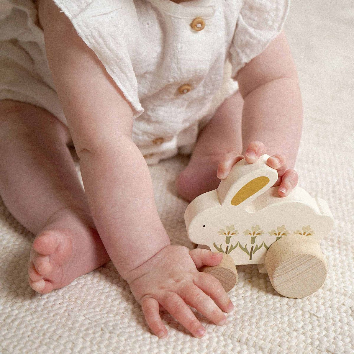 Child seated beside a wooden bunny on wheels, with a hand resting on its long ear.