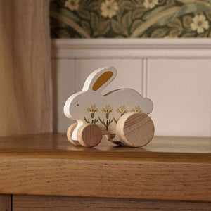 Cream floral wooden bunny toy with natural wood wheels displayed on a wooden cabinet.