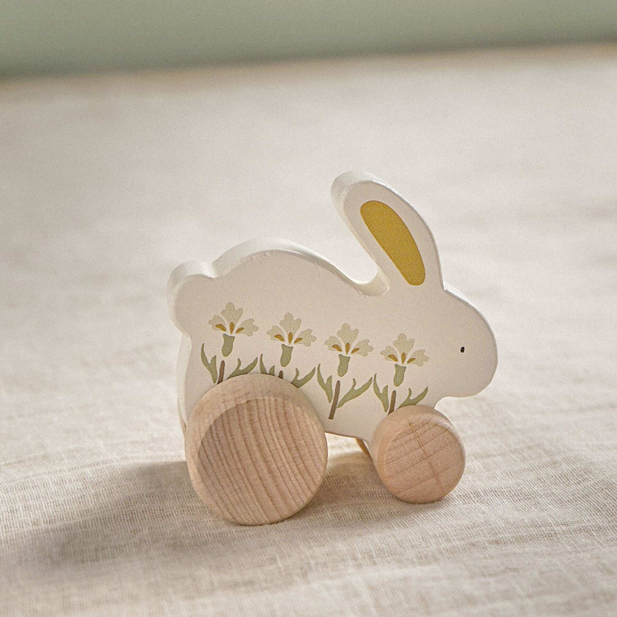 Reverse side of the floral wooden rabbit toy resting on neutral linen.