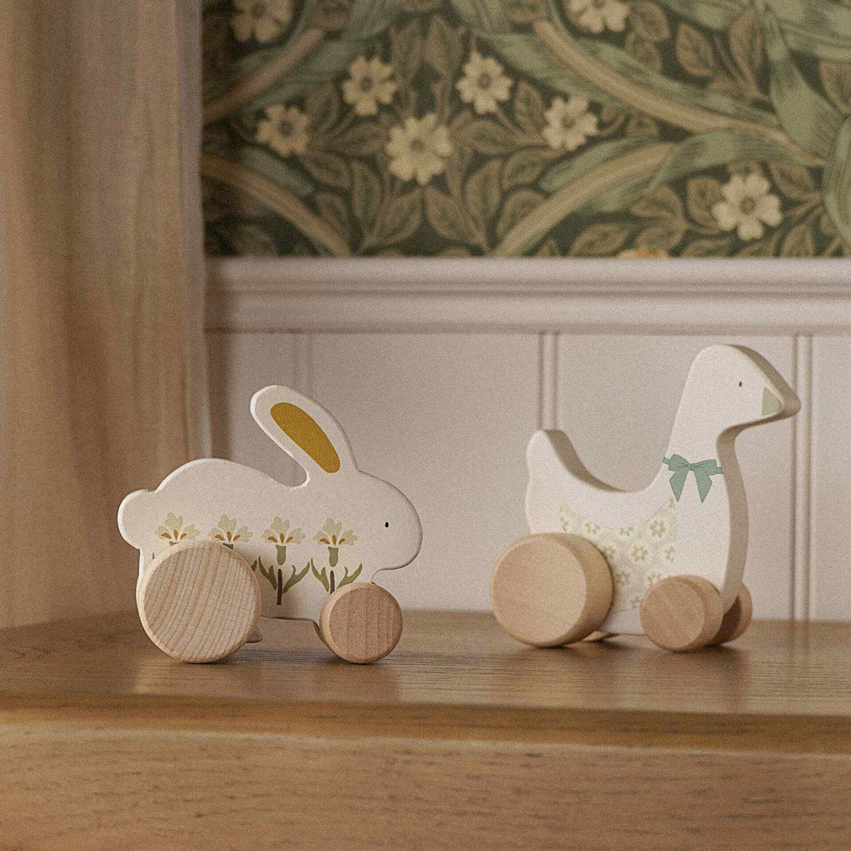 Wooden bunny and goose toys on wheels displayed together on a nursery cabinet.