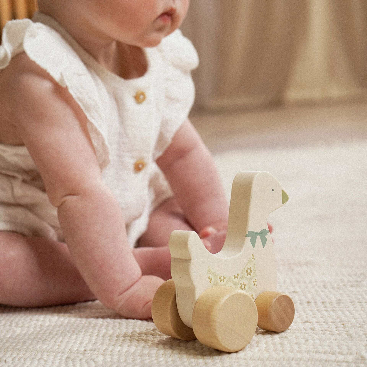 Child seated beside a cream wooden goose toy with floral detail and natural wood wheels.