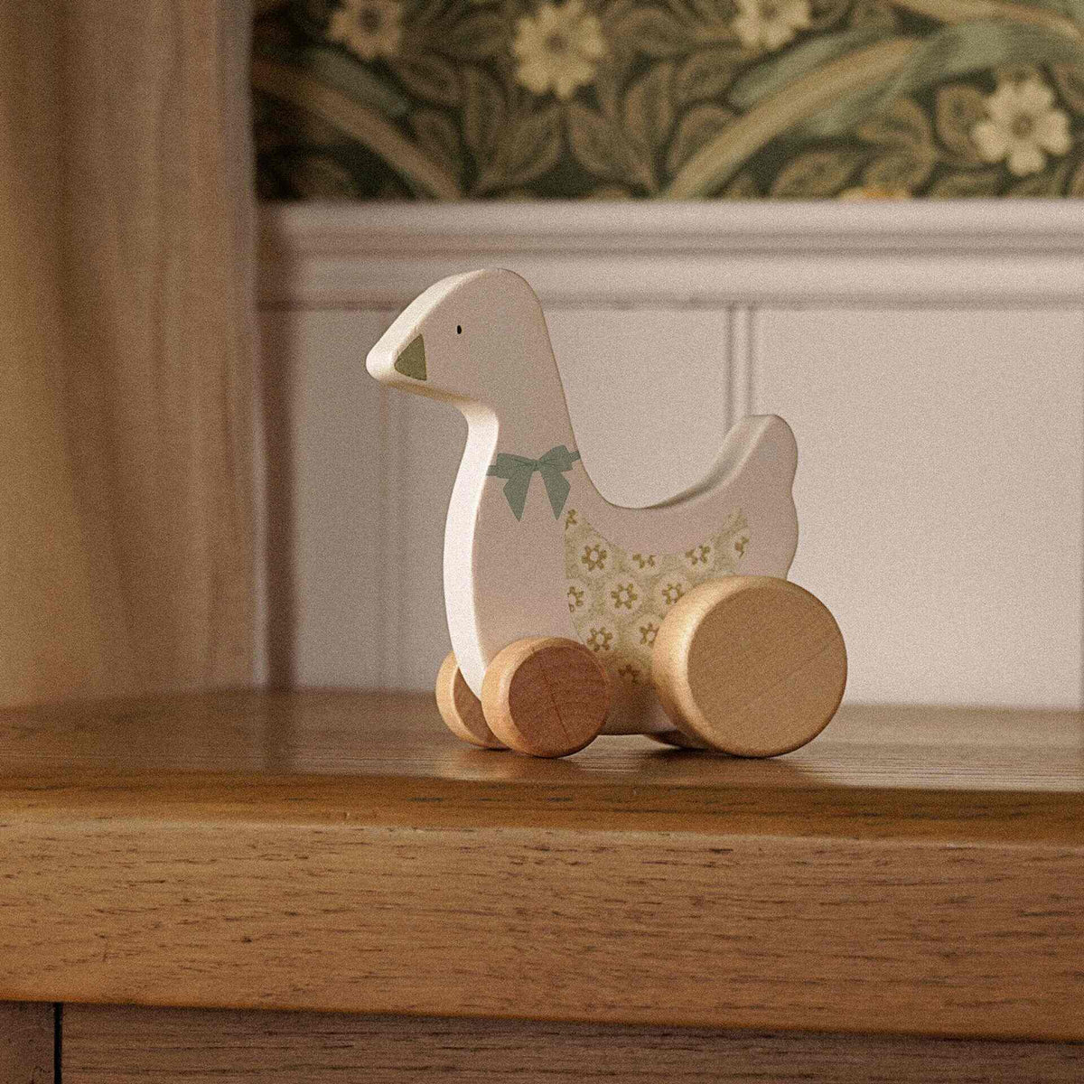 Cream wooden goose on wheels with a painted bow displayed on a wooden cabinet.