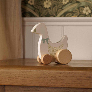 Cream wooden goose on wheels with a painted bow displayed on a wooden cabinet.