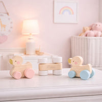Wooden duck push toys with pink, white and blue wheels on a nursery dresser.
