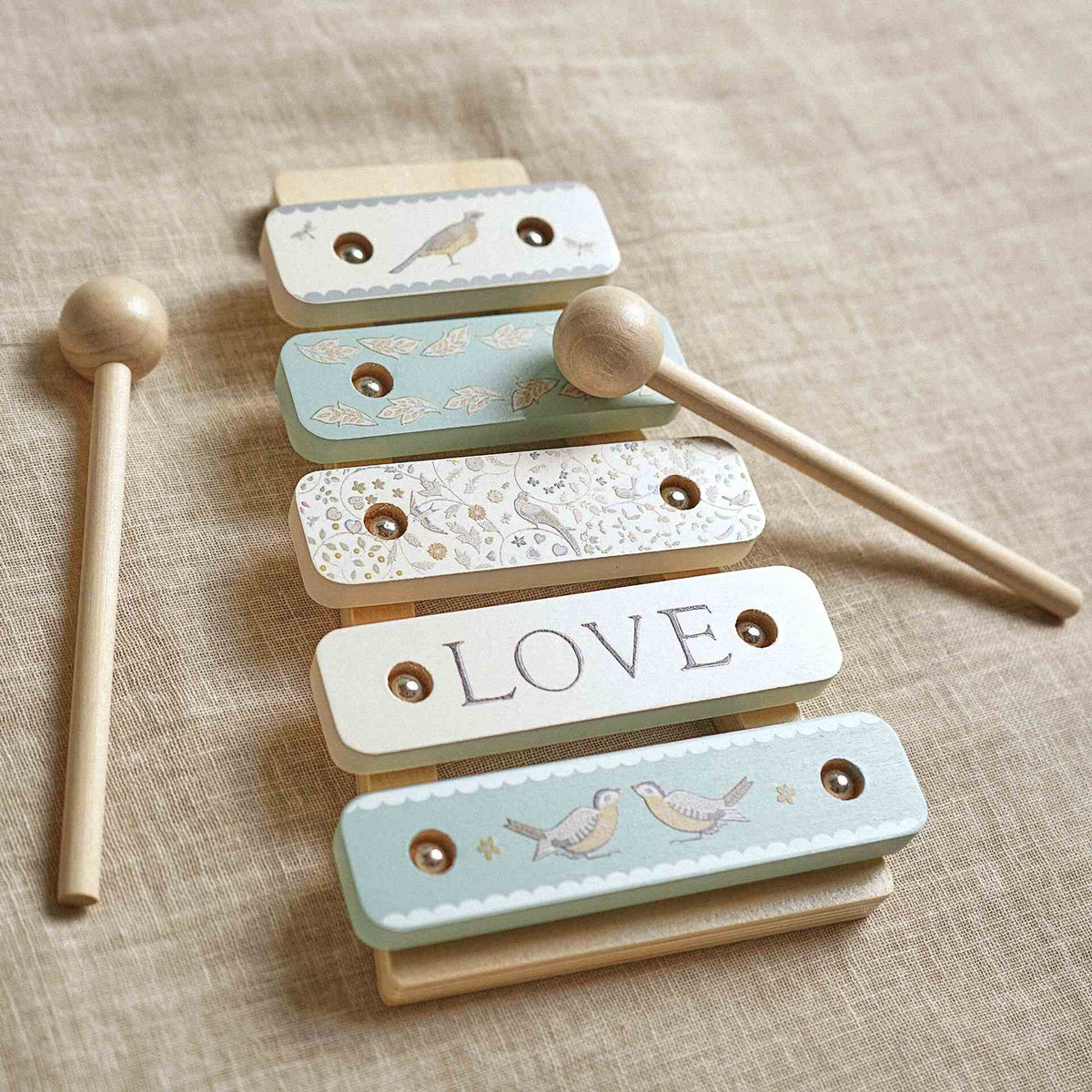 Five-bar wooden toy xylophone with bird and floral patterns and two mallets on linen