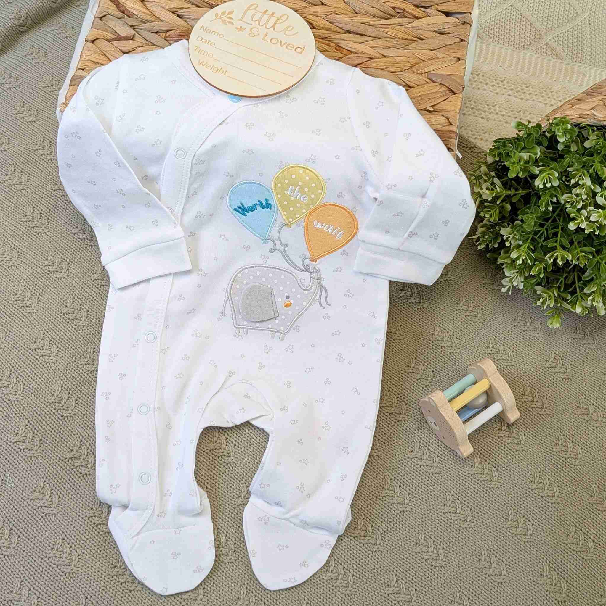 White baby sleepsuit which reads worth the wait and has an elephant.