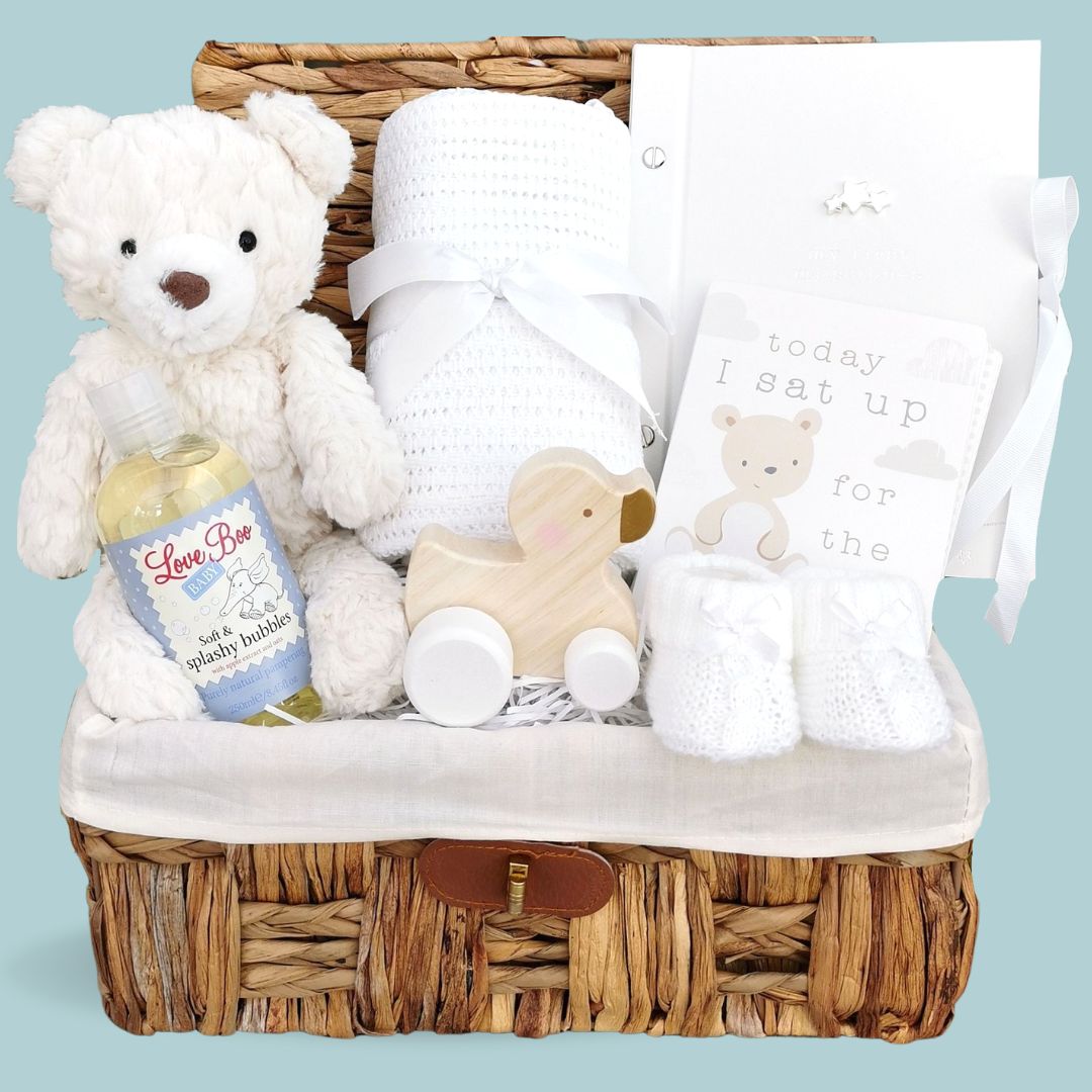 Baby gift hamper basket with white teddy, white blanket, record book and baby toy.