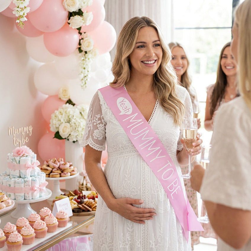 Mum-to-be in a white dress wearing a pink sash with white Mummy to Be lettering.