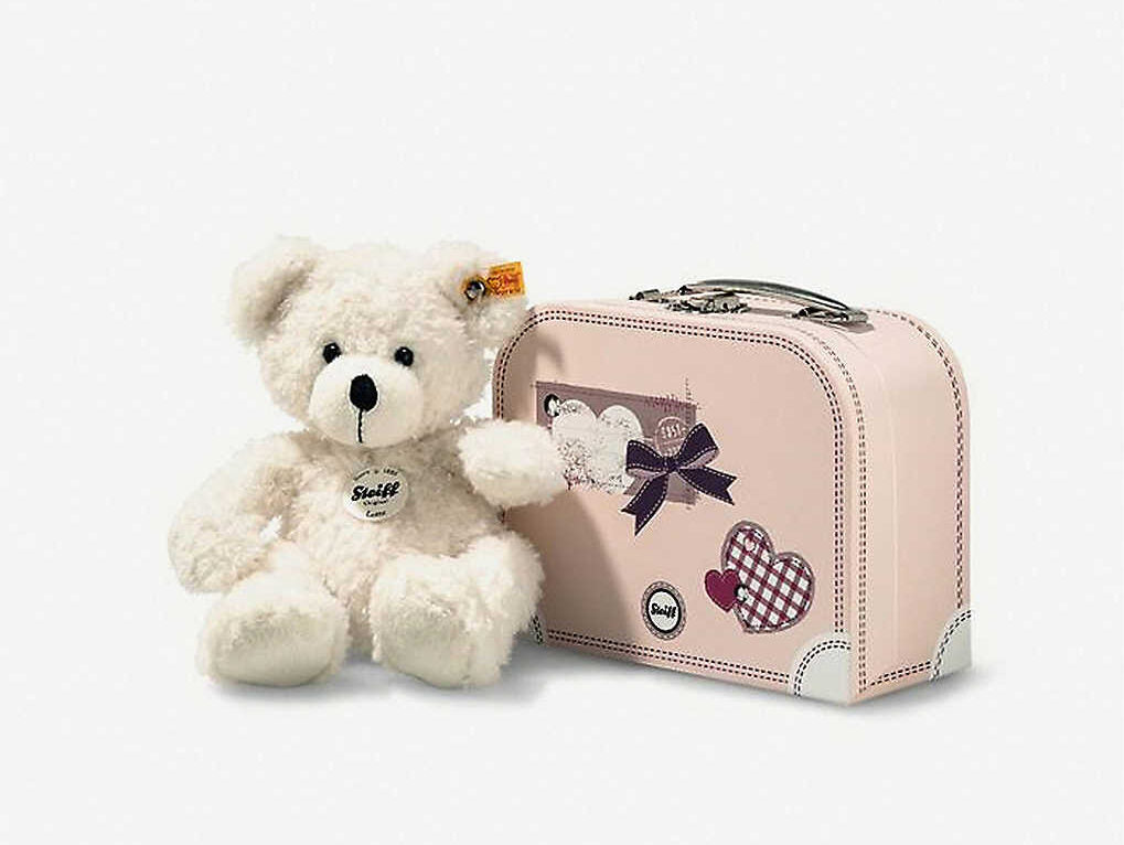 White soft teddy bear toy, sitting on a pink suitcase. Lotte has the yellow Steiff logo tag in her ear.